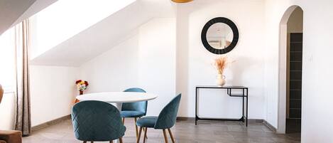 A modern interior with a round dining table, blue upholstered chairs, a black console table with a vase, and a large mirror on the wall.
