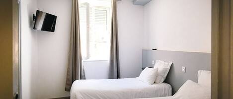 Habitación de hotel con dos camas, un televisor de pantalla plana montado en la pared y una ventana con cortinas.