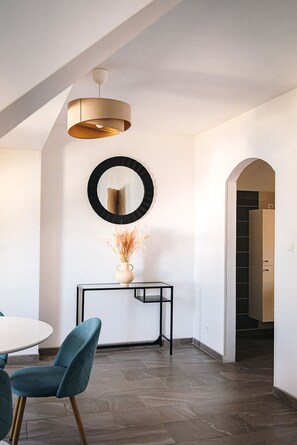 Un interior moderno con una zona de comedor, un espejo redondo, un jarrón con plantas secas y una escalera que sube a otro nivel.