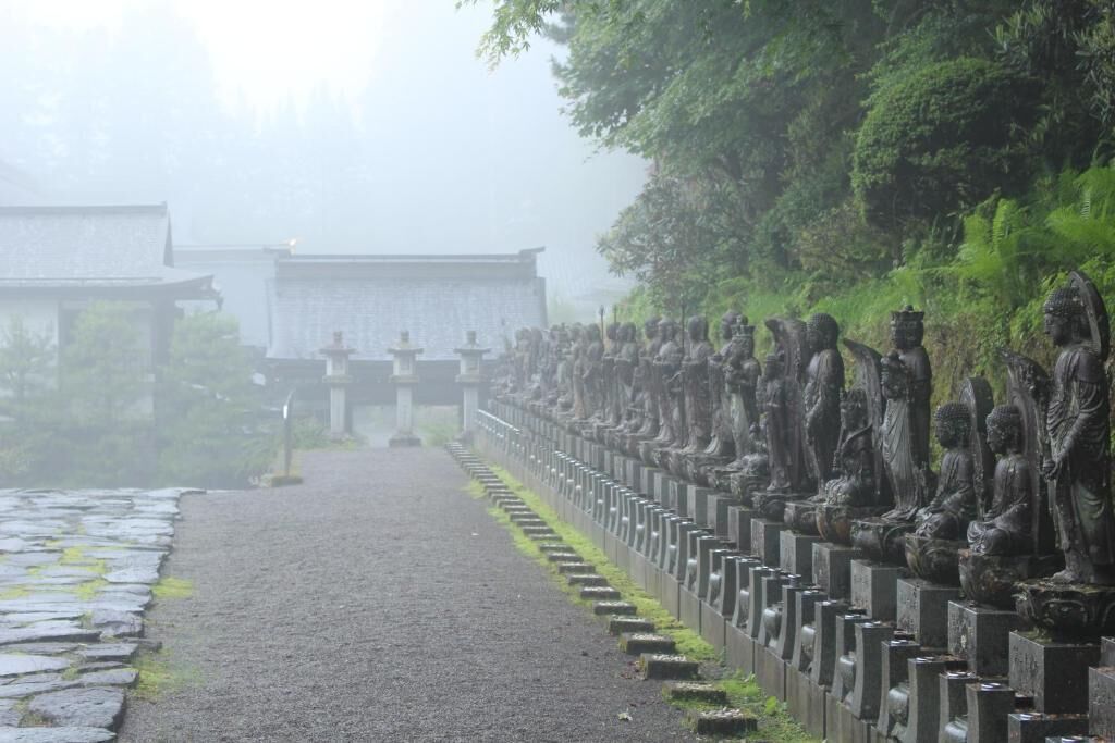 A pathway lined with statues leading to a traditional building.