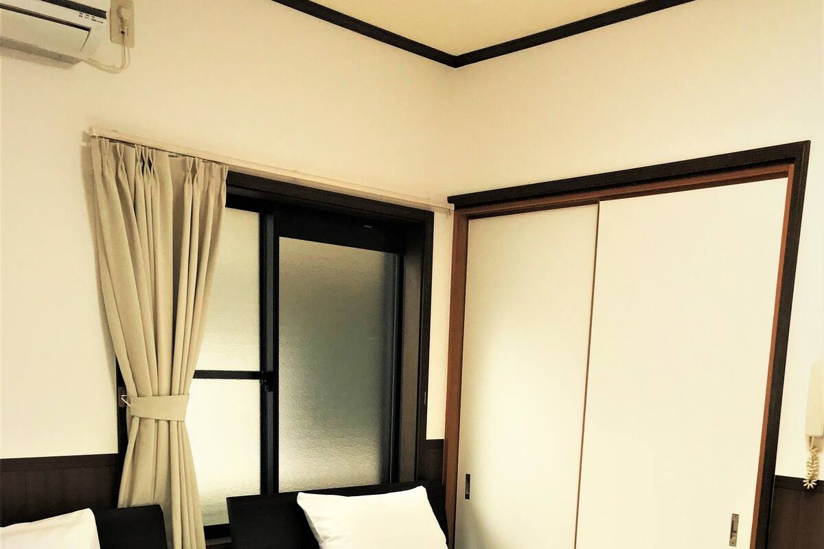 A hotel room with a large bed, a window with curtains, a wardrobe, and a wall-mounted air conditioning unit.