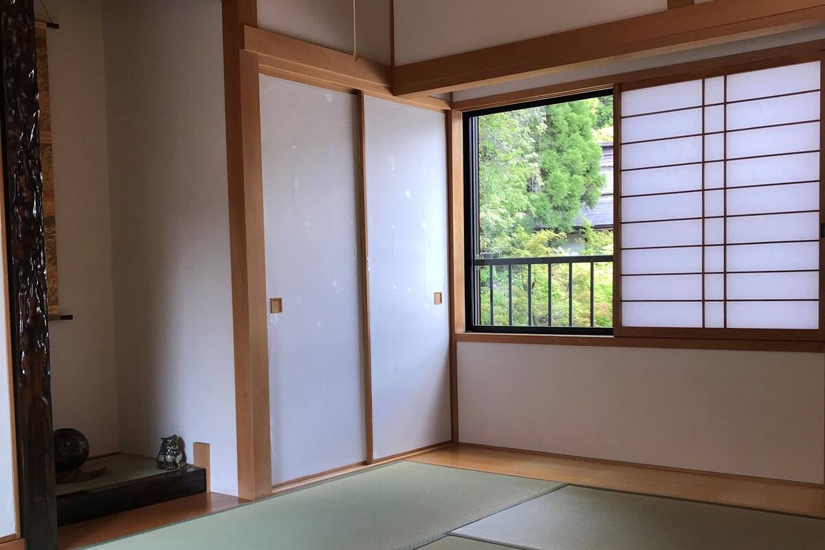 A traditional Japanese room with tatami flooring, sliding doors, and a view of greenery outside.