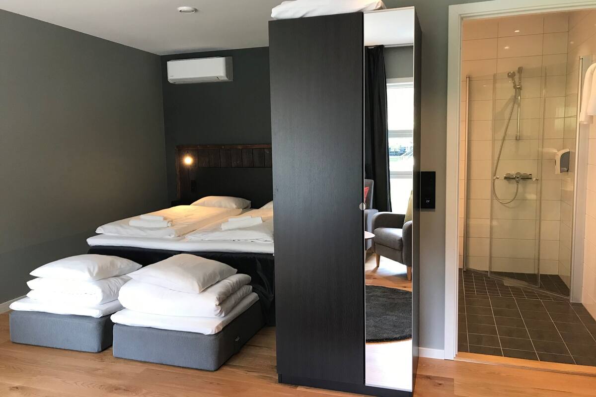 Ein modernes Hotelzimmer mit einem großen Bett, einer separaten Sitzecke, einer Dusche und einer sichtbaren Klimaanlage.