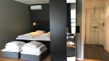 Ein modernes Hotelzimmer mit einem großen Bett, einer separaten Sitzecke, einer Dusche und einer sichtbaren Klimaanlage.