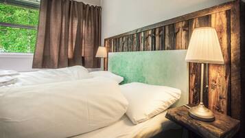 Una cama bien hecha con sábanas blancas, cabecera de madera y lámpara de noche.