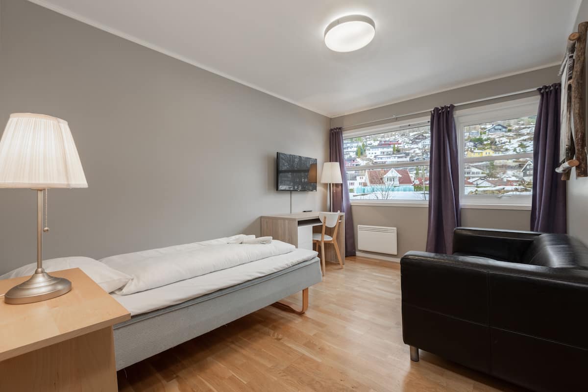 Ein modernes Hotelzimmer mit Bett, Schreibtisch, Stuhl und einer schwarzen Ledersofa.