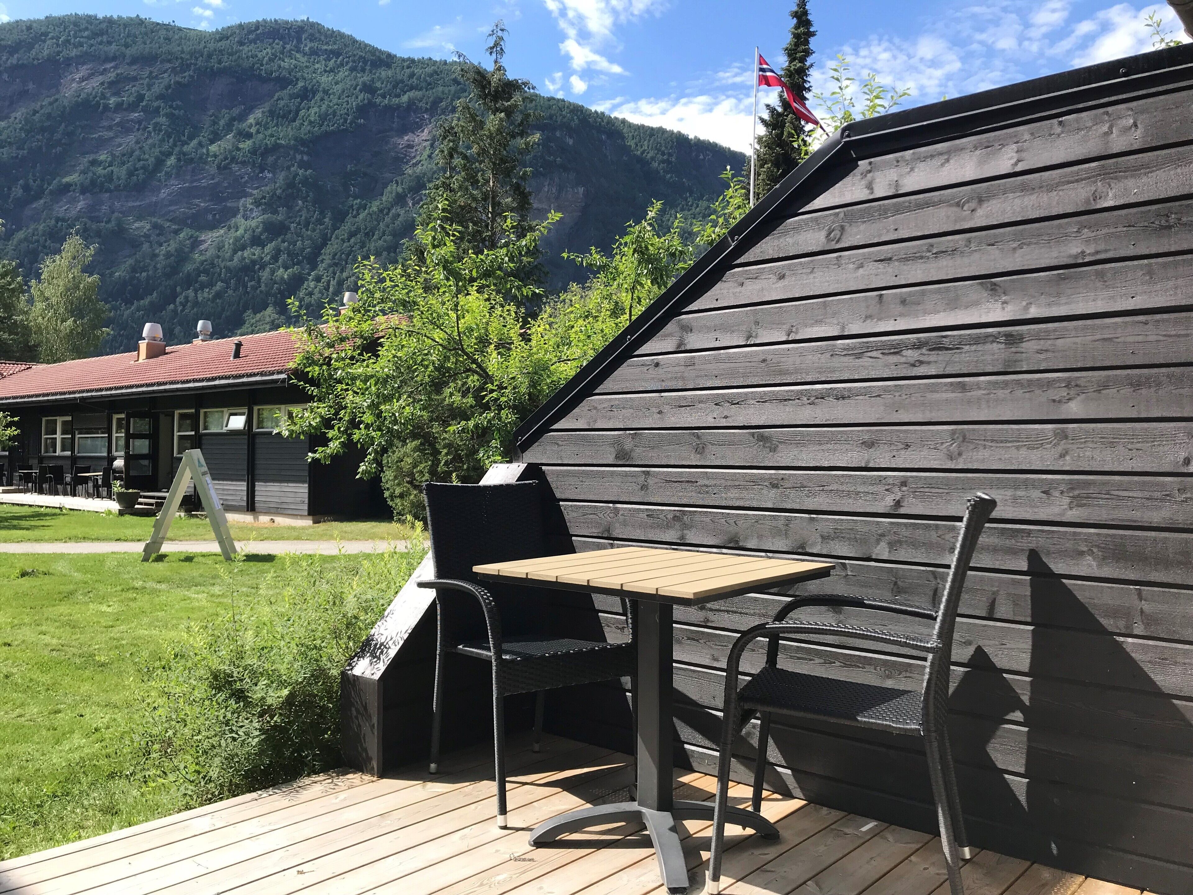 A wooden deck with a table and chairs, a building with a red roof, and a flag.