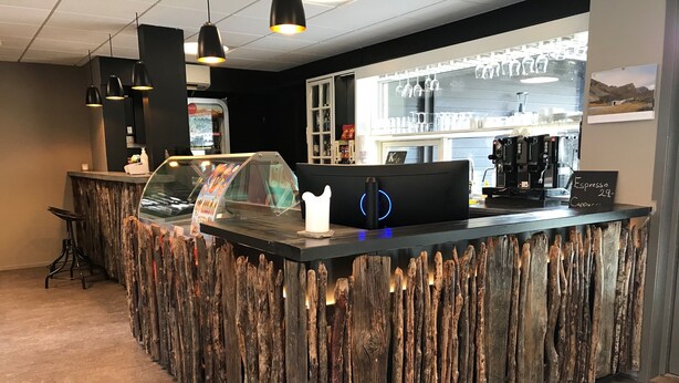 Een bar met een rustieke houten toonbank, een koffieapparaat en een etalage met drinkglazen.