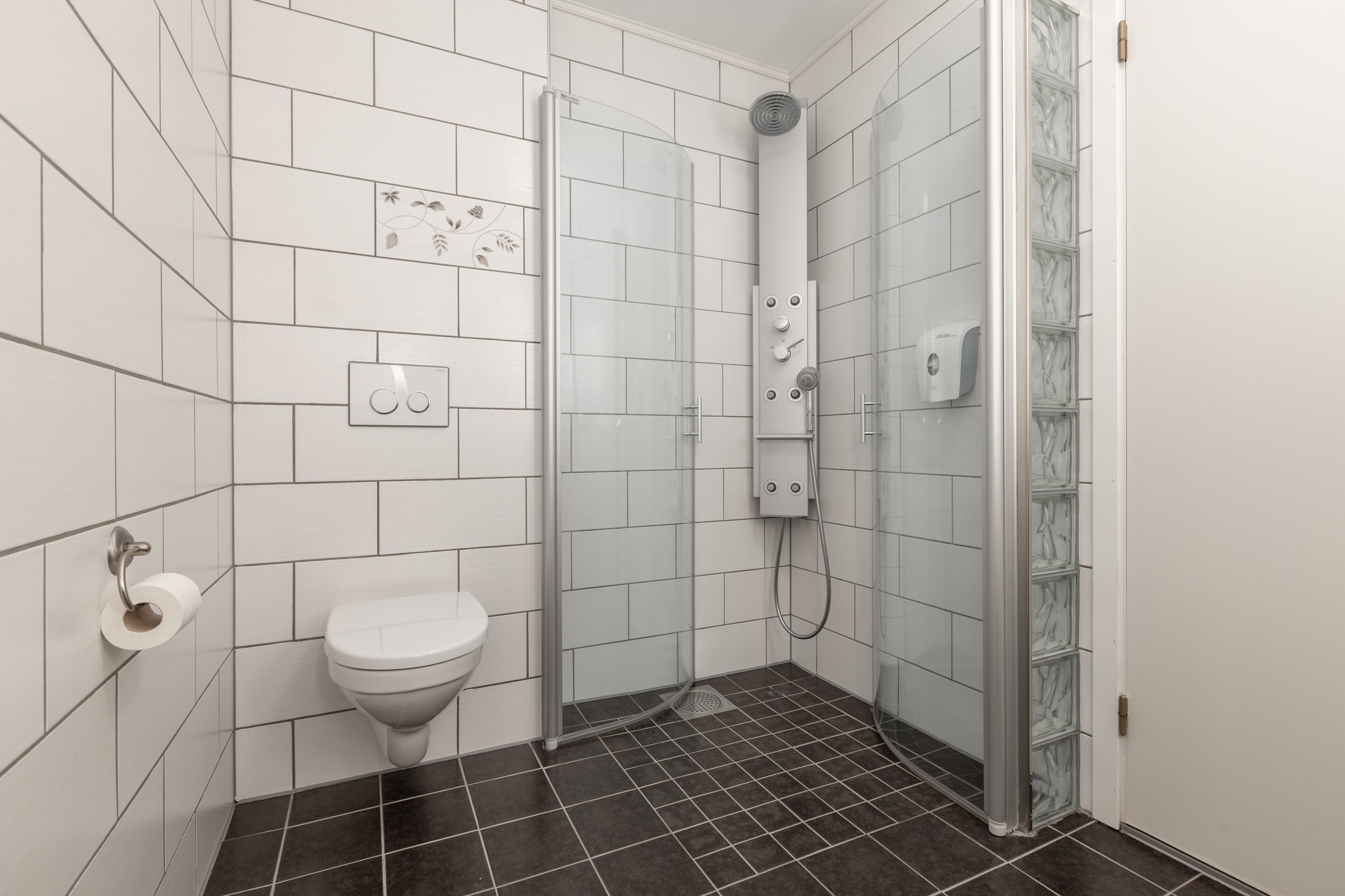 Un baño con azulejos blancos, un inodoro, una ducha con puerta de vidrio y un perchero para toallas.