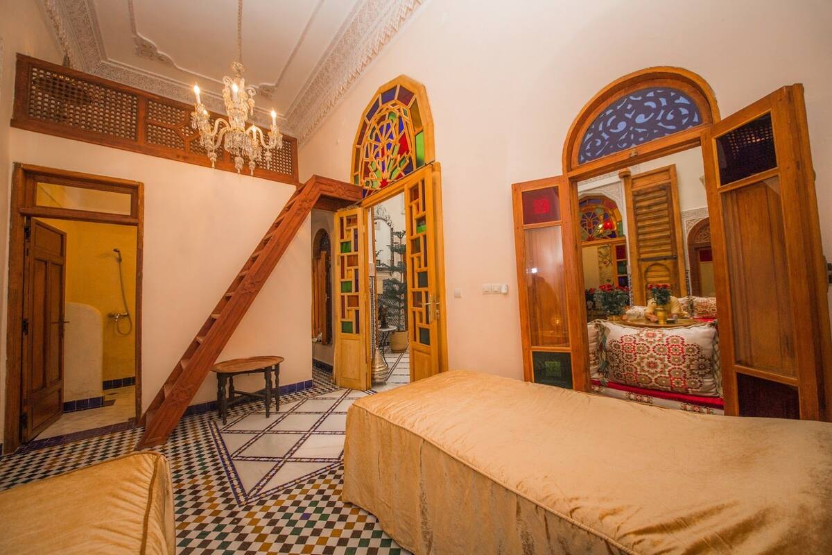 A room with a checkered floor, a bed, a wooden staircase, and a chandelier.