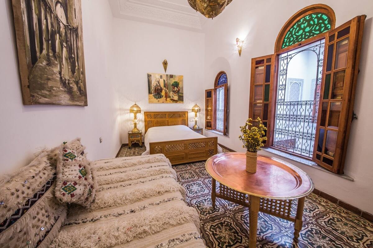 A traditional room with a bed, a sofa, a table with a vase, and a painting on the wall.
