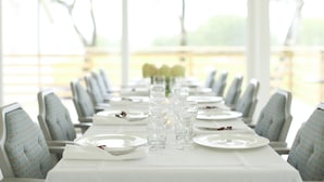 A dining table set with plates, glasses, and cutlery, with chairs on either side.