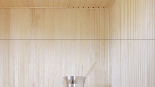 A sauna with wooden benches and a metal bucket.