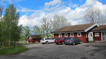 A red building with a tiled roof, a parking lot with several cars, and surrounding trees.