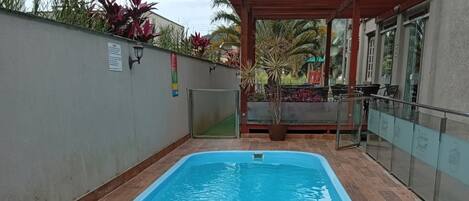 Una piscina con dos sillones de mimbre y una mesita, rodeada por una zona de patio con baldosas.