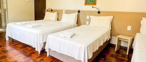 A hotel room with two beds, wooden flooring, a door, and a small bedside table.