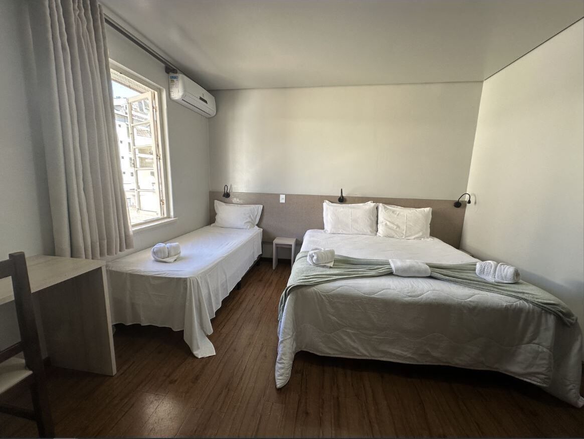 Une chambre d’hôtel avec deux lits simples, une petite table, une chaise et une fenêtre avec des rideaux.