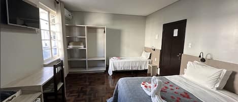 Una habitación de hotel con cama, escritorio, silla, armario y televisor.
