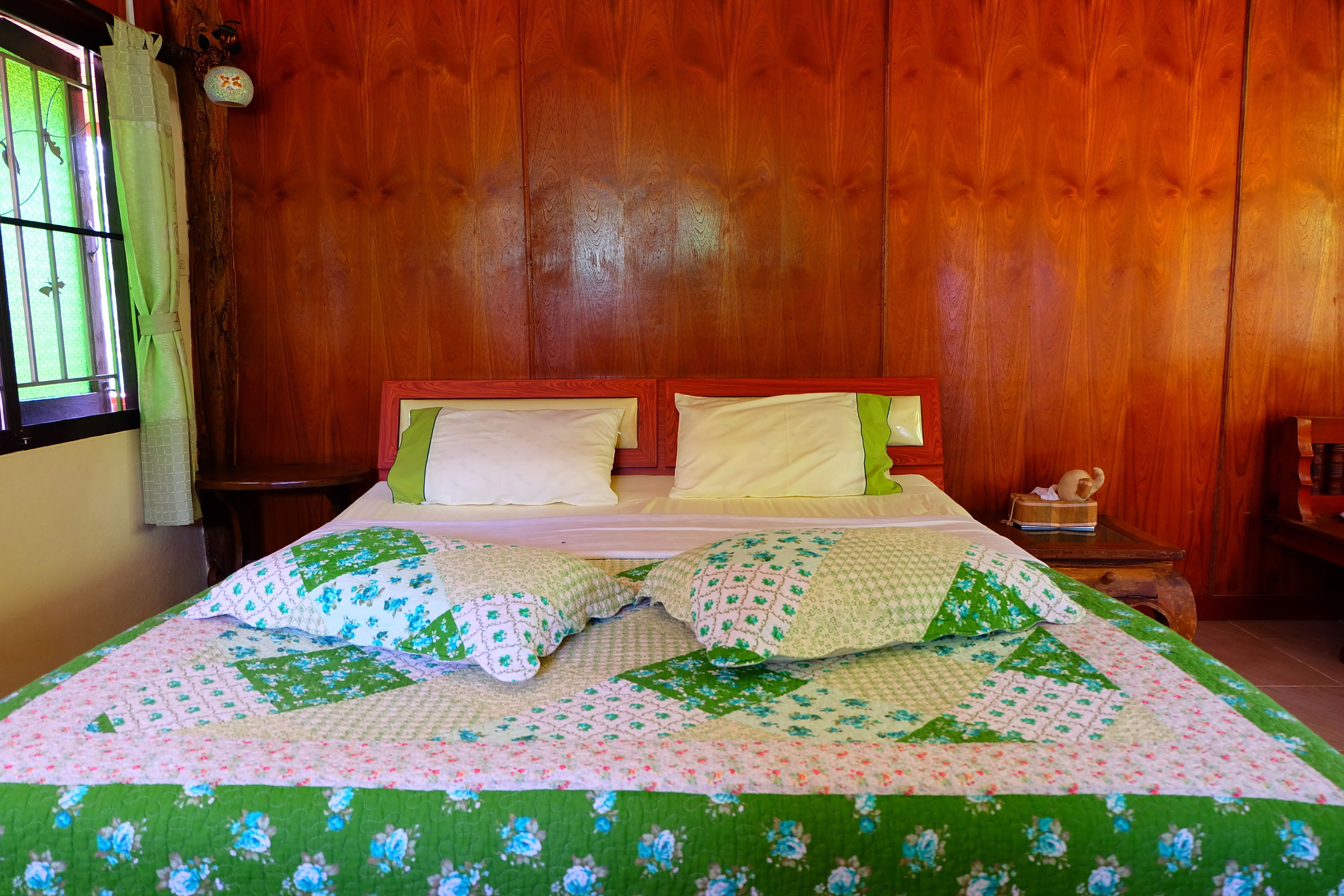 Una cama con ropa de cama floral, un cabecero de madera y una mesita de noche con lámpara.