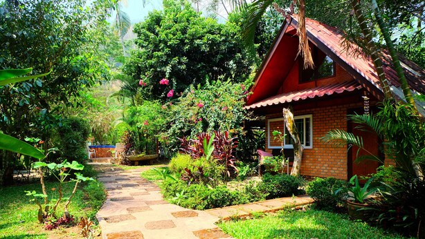 A garden pathway leading to a brick house with a red roof.