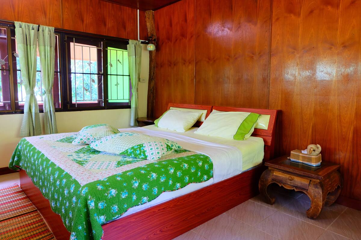 A wooden-paneled room with a bed, curtains, and a small wooden nightstand.