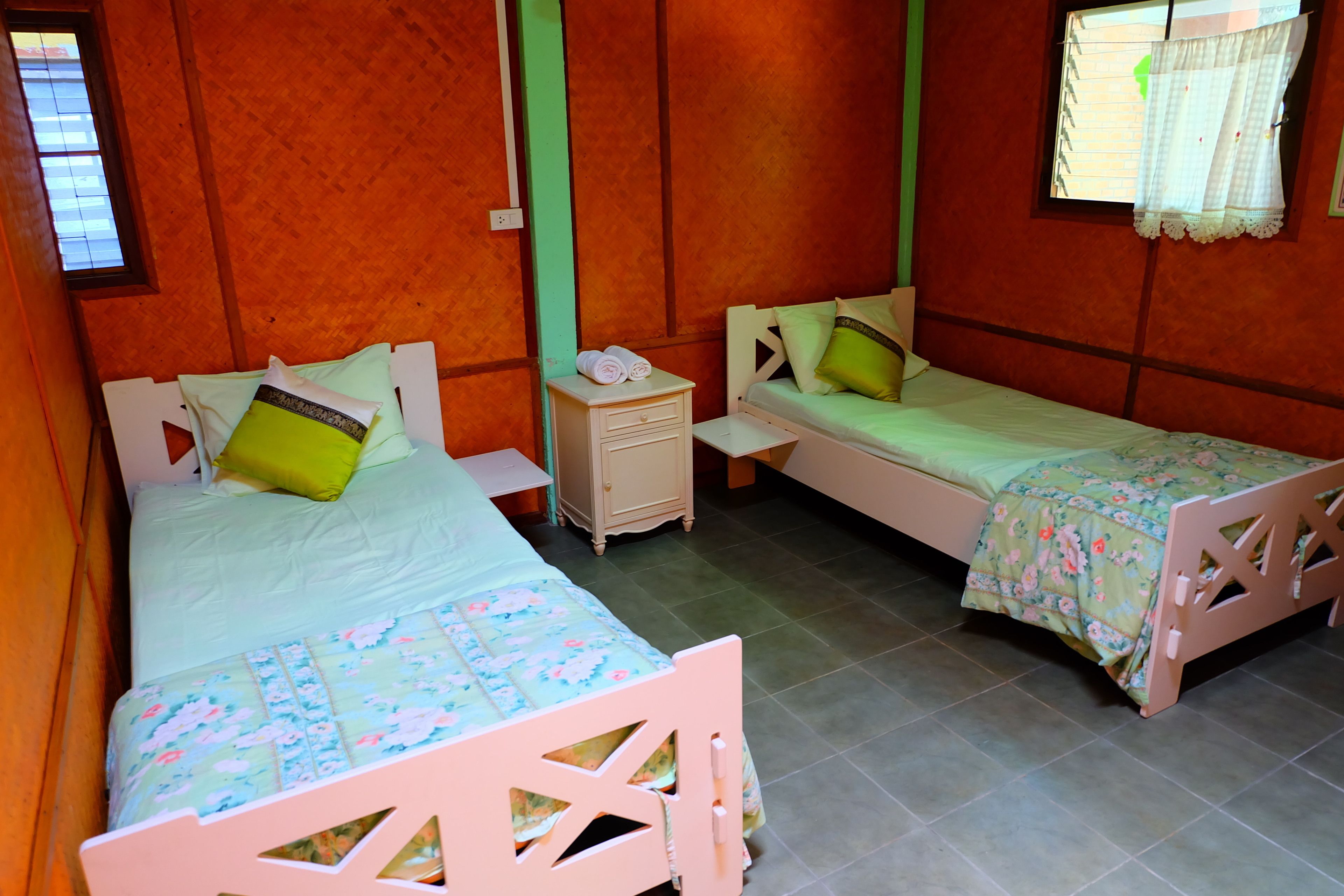 A room with two beds, each with a pillow and a nightstand.