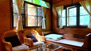 A room with wicker furniture, a glass table, and a bed with a white mattress.