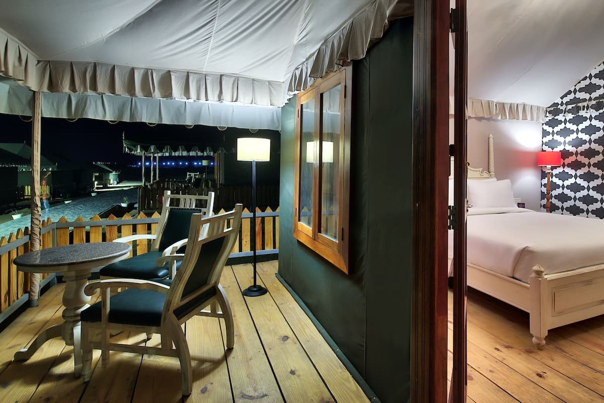 Una habitación con cama, piso de madera, balcón con mesa y sillas y vista al exterior.