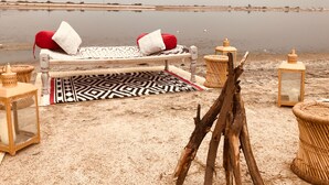 Un entorno de playa con un banco de madera, un tapete estampado y dos faroles.