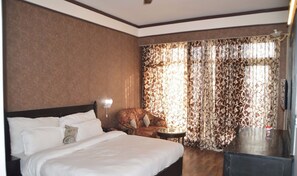A hotel room with a large bed, a chair, a small table, and curtains with a floral pattern.