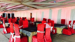 A banquet hall with rows of tables and chairs, a ceiling with a geometric pattern, and a pink curtain backdrop. - Sun N Star (Dehradun)