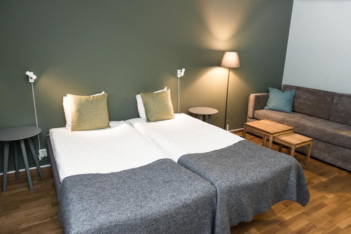 A room with two beds, a small round table, a sofa, and a lamp.