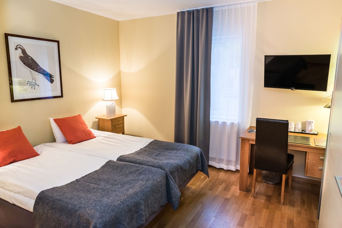 A hotel room with two beds, a desk, a chair, a TV, and a framed picture on the wall.