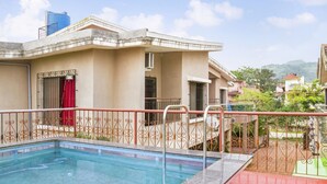 A residential building with a swimming pool, a red door, and a balcony with a metal railing.
