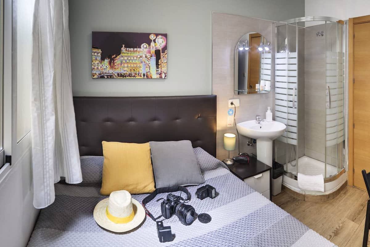A hotel room with a bed, a nightstand, a shower, and a painting on the wall.