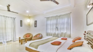 Une chambre à coucher avec un lit, deux fauteuils en osier, un ventilateur de plafond et une grande fenêtre avec des rideaux.