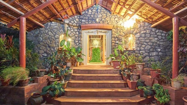 A stone building with a wooden staircase leading to a door, surrounded by potted plants. - GuestHouser 1 BR Villa 520d (Mawal)