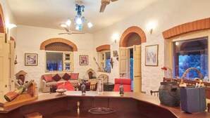 A spacious living room with a large wooden coffee table, a sofa, and a dining table. There are arched windows and a ceiling fan. - GuestHouser 1 BR Villa 520d (Mawal)