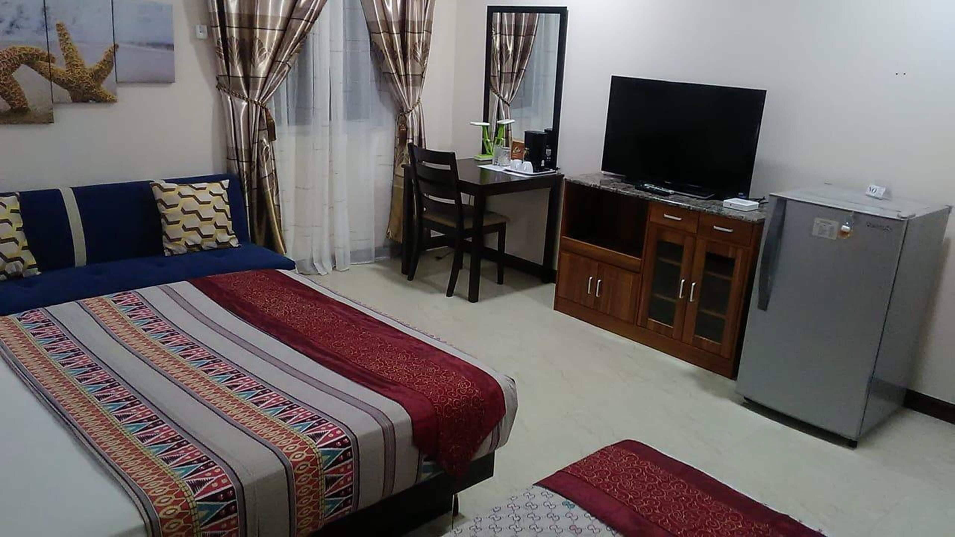 A hotel room with a bed, a desk with a chair, a television, and a wardrobe.