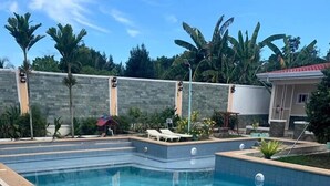 A swimming pool with a tiled deck, surrounded by a stone wall and palm trees. - Venezia Suites Resort (Panglao)