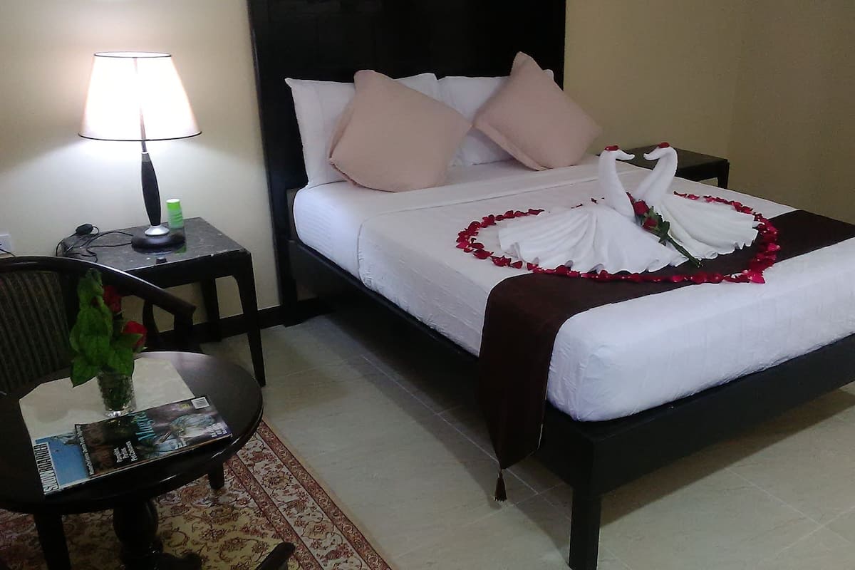 A neatly made bed with white linens, a brown headboard, and a decorative swan and rose arrangement on the bed.