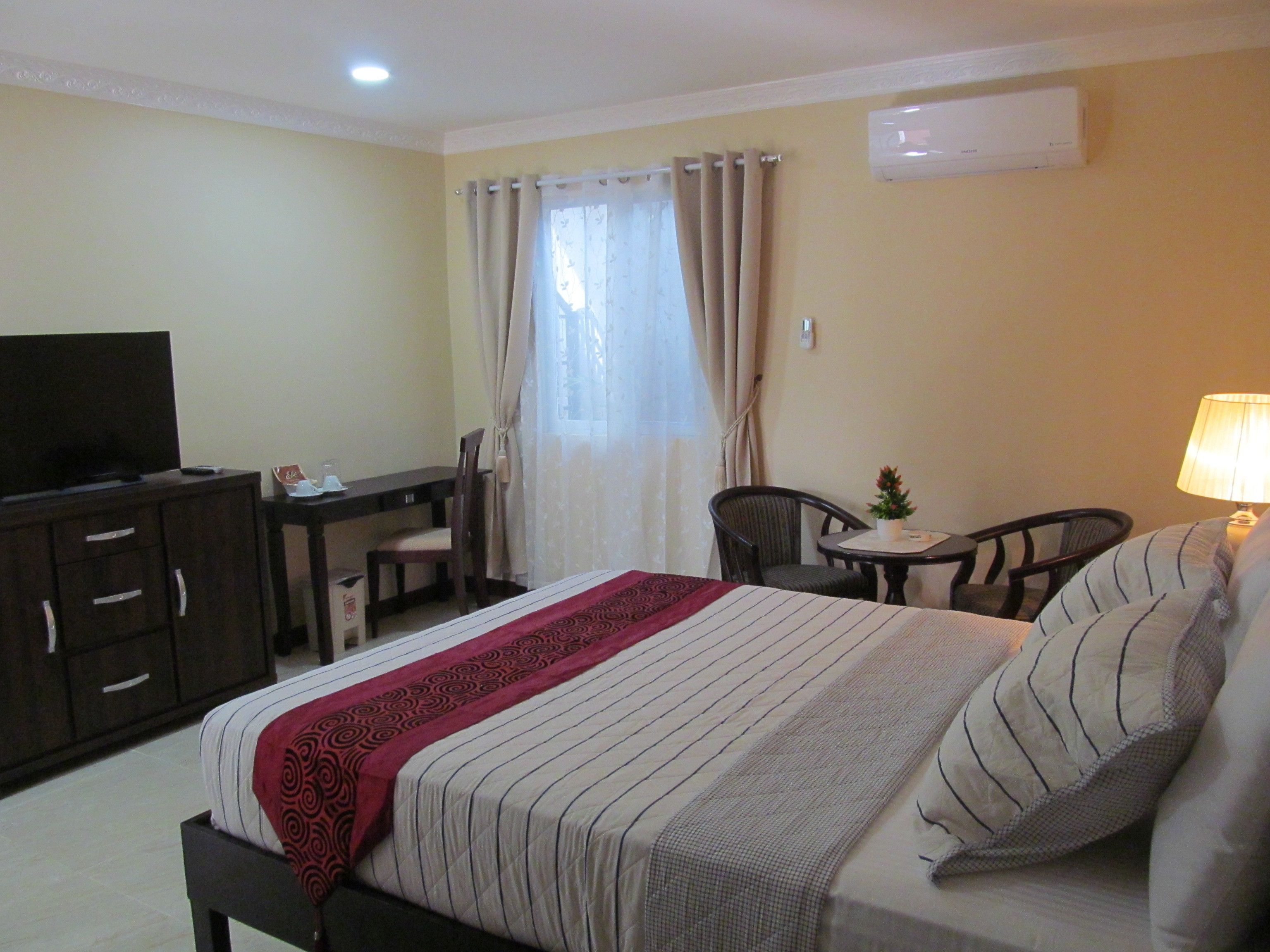 A hotel room with a bed, a desk, a chair, a television, and a lamp.
