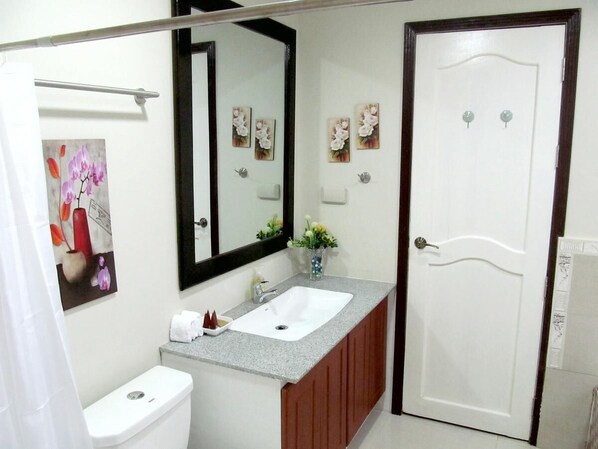 Une salle de bain avec des toilettes blanches, un lavabo avec un miroir au-dessus et une porte dotée d’une poignée.
