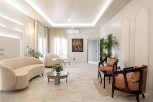 Uma sala de estar moderna com um sofá bege, uma poltrona de madeira e uma mesa de centro.