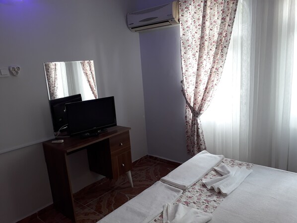 A bedroom with a bed, a desk with a television, a mirror, and a window with curtains.