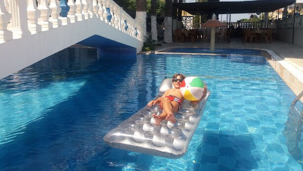 Piscina com água azul cristalina, um guarda-corpo branco e uma pessoa deitada em um boi inflável.