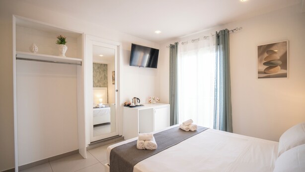 A hotel room with a bed, a TV, a desk with a computer, a mirror, and a bathroom visible through an open door.