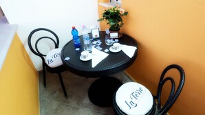 A small round table with chairs, a potted plant, and scattered items like a water bottle, glasses, and napkins.