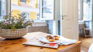 Una mesa de madera con una cesta tejida llena de flores, un plato con tres pasteles y una revista.