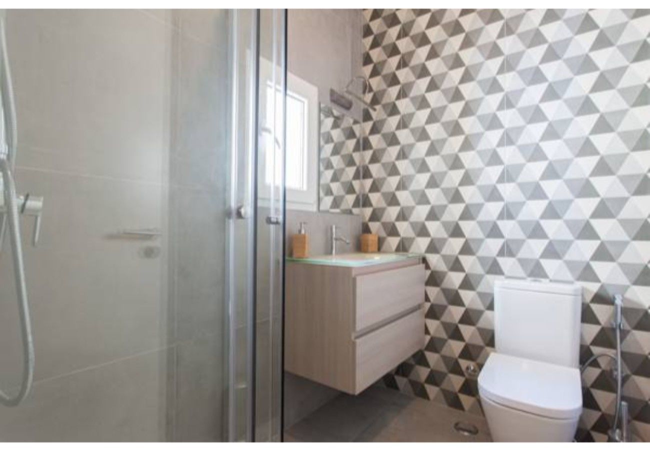 A bathroom with a geometric patterned wall, a glass shower enclosure, a wooden vanity, and a white toilet.